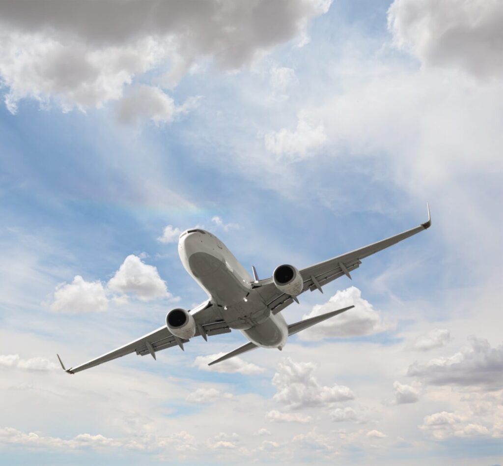 A commercial airplane is flying upward through a partly cloudy sky, viewed from below with its landing gear retracted.