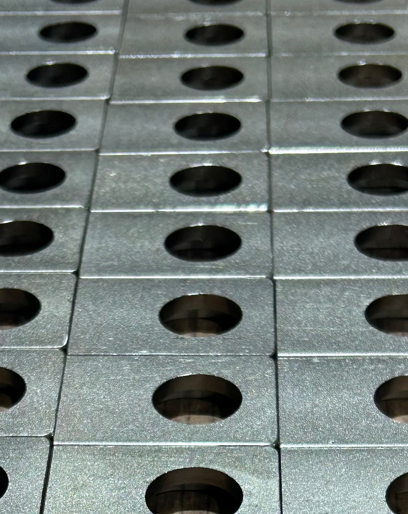 A close-up view of a grid of metallic plates, each with a circular hole in the center, arranged in neat rows and columns.