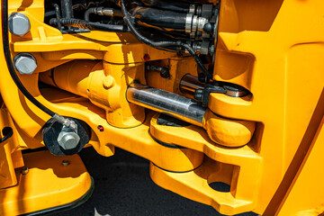 Close-up view of yellow hydraulic machinery parts, showing metal pistons, hoses, and bolts, highlighting the mechanical components and industrial design.