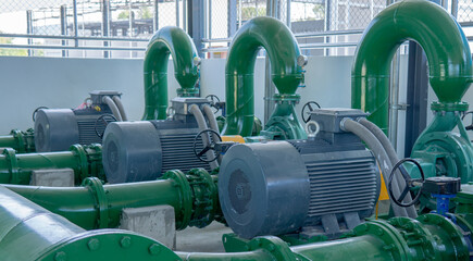 Four large green industrial water pumps with electric motors are installed in a plant, connected by pipes and resting on concrete bases in a clean, indoor facility.