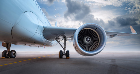 Close-up of a commercial airplanes turbine engine and landing gear on an airport runway with a cloudy sky in the background.