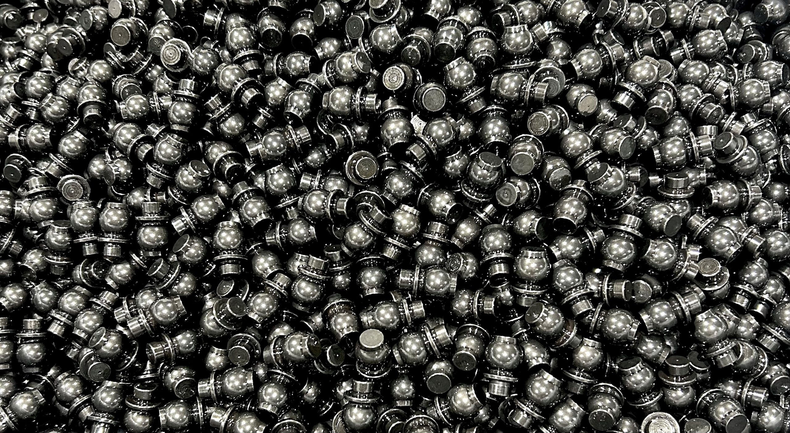 A large pile of shiny, black, cylindrical plastic caps or plugs, densely packed together, filling the entire image.
