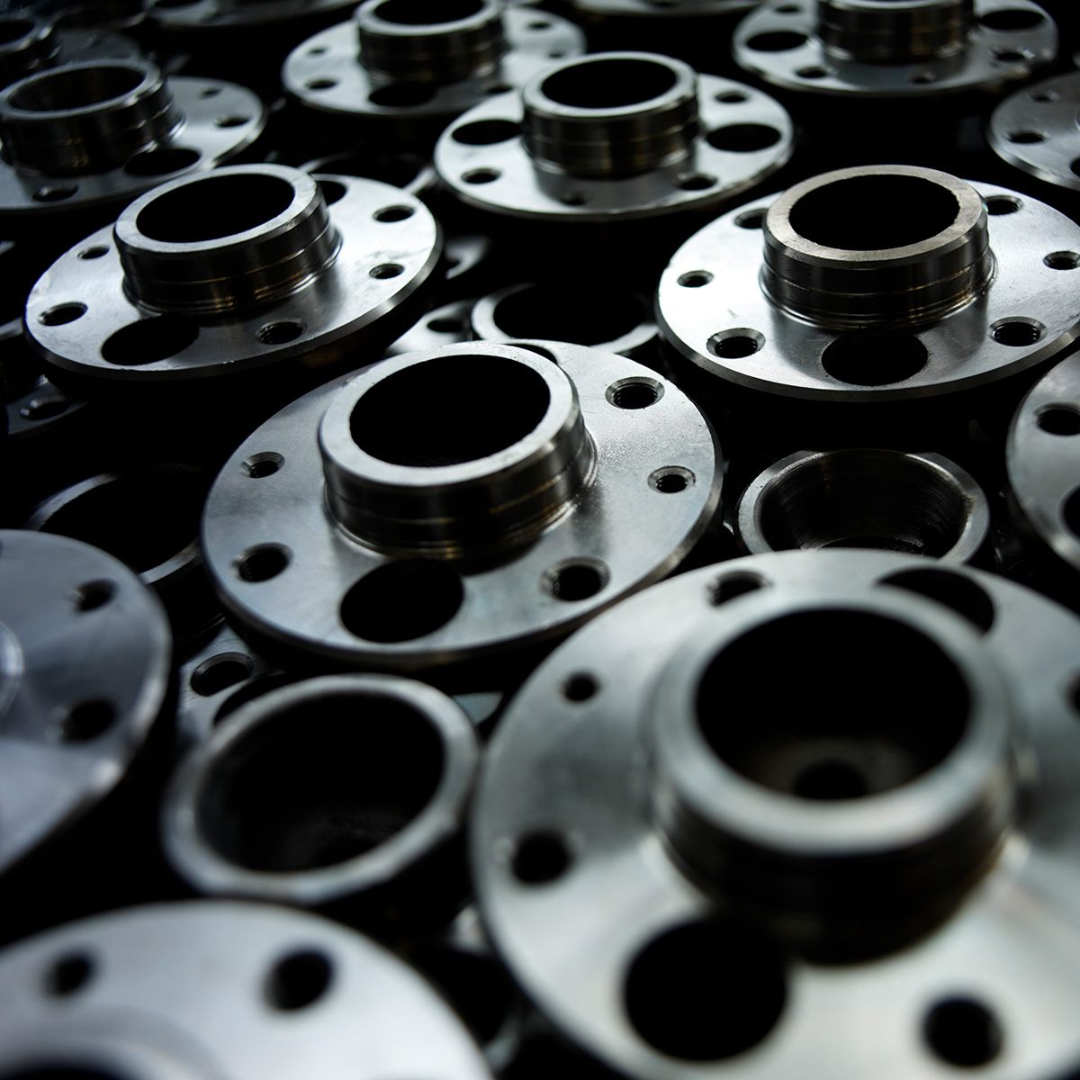 Close-up of multiple shiny metal flanges with circular holes, stacked and overlapping in an industrial setting.
