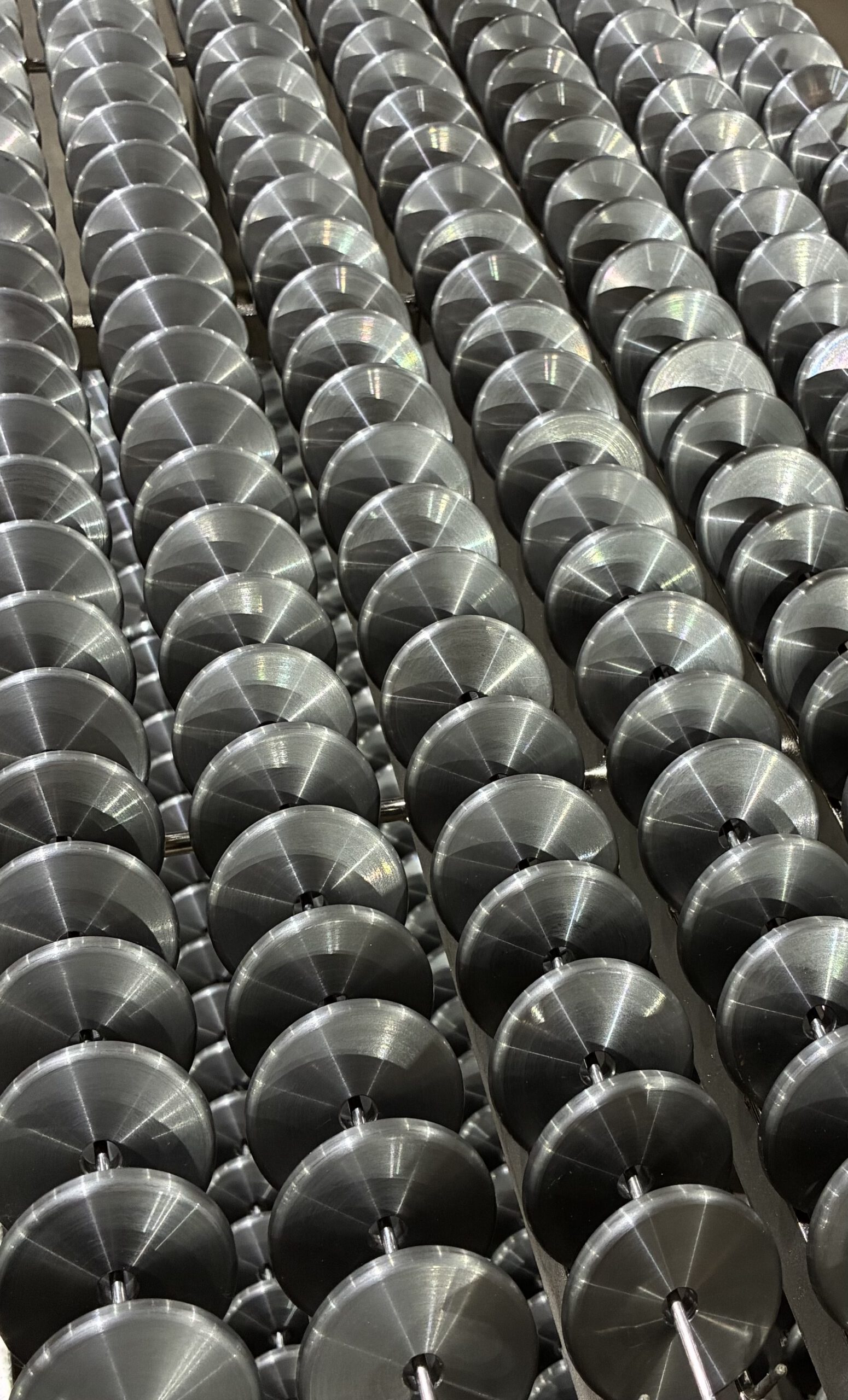 Rows of shiny, metal, disc-like machine parts are arranged in parallel lines, creating a repeating, industrial pattern.