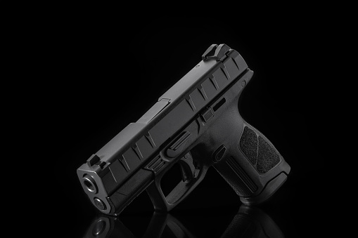 A black semi-automatic handgun is displayed on a reflective black surface with a dark background.